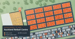 Illustrated aerial map of the Auckland Netball Centre at Ngahue Reserve, St Johns, showing a busy indoor arena with its roof cut away, rows of floodlit orange outdoor courts dotted with players, and a large car park, with a map key labelled Auckland Netball Centre.